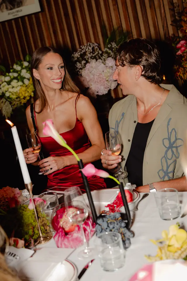 A candid shot of a man and a woman smiling and interacting at a beautifully decorated table during an evening event. The table is adorned with various floral arrangements, candles, and a sophisticated place setting, suggesting a celebratory or launch occasion.